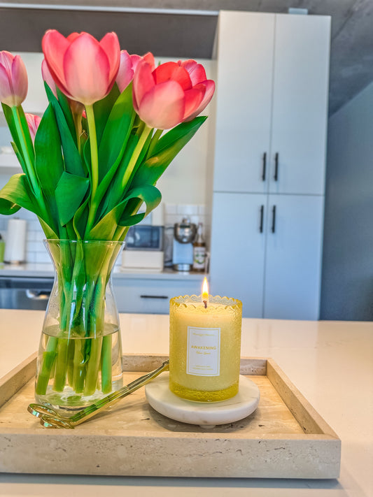Bouquet of pink tulips in a vase with a lit candle on a wooden tray in a kitchen.