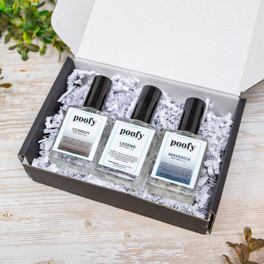 Three small perfume bottles from the brand poofy, labeled 'Corcey', 'Legend', and 'Maverick', arranged in white crinkle paper inside an open black gift box on a light wood surface.
