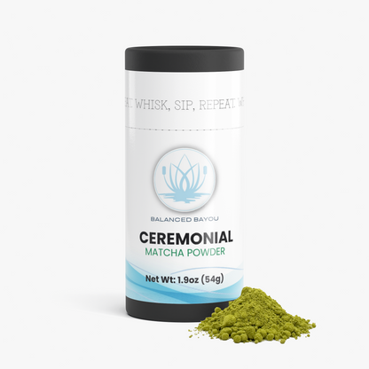 A white cylindrical container of Balanced Bayou Ceremonial Matcha Powder with a black lid, shown on a light gray background with a small pile of green matcha powder in front.