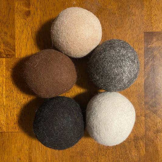 Five felt balls in beige, brown, gray, black, and white on a wooden surface.