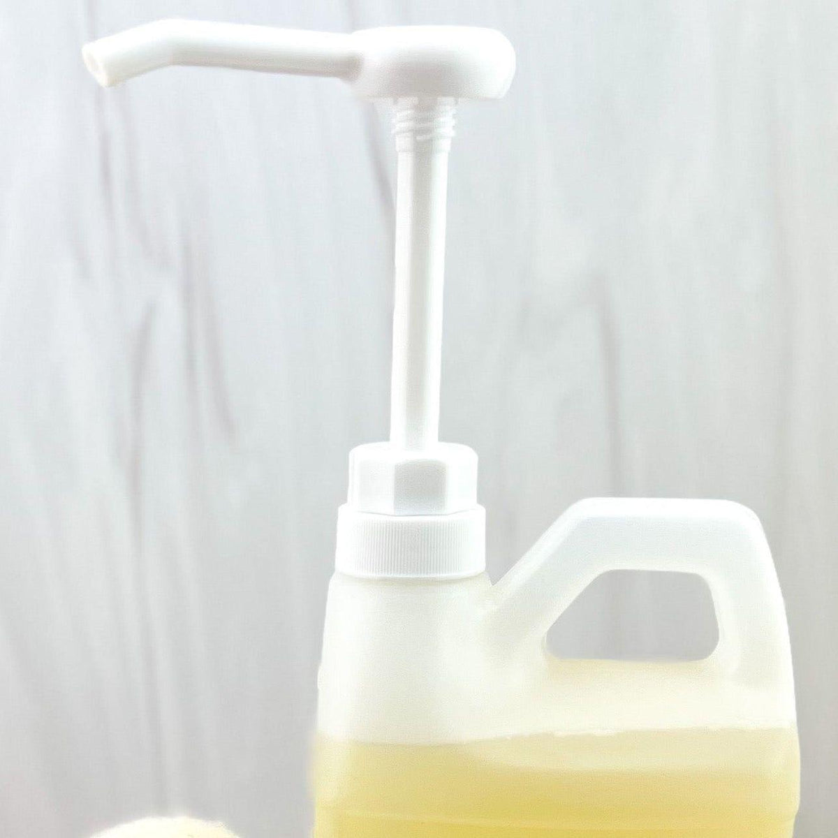 A translucent white plastic bottle with a built-in pump dispenser and carry handle, partially filled with pale yellow liquid, shown against a soft light gray background.