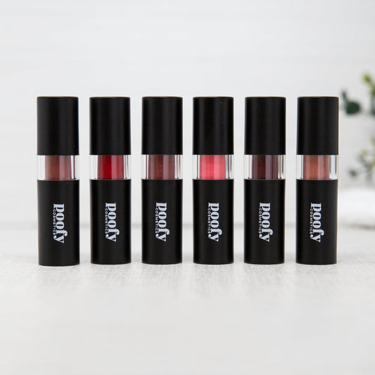 Six tubes of glossy liquid lipstick in different shades are lined up on a white surface. Each tube has a black cap and a black body with the brand name 'poopy' printed in white, and a clear section showing the lipstick color inside.