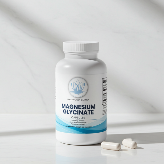A white bottle of Balanced Bayou Magnesium Glycinate Capsules with two capsules resting in front, set on a light marble surface with a matching marble background.