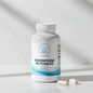 A white bottle of Balanced Bayou Magnesium Glycinate Capsules with two capsules resting in front, set on a light marble surface with a matching marble background.