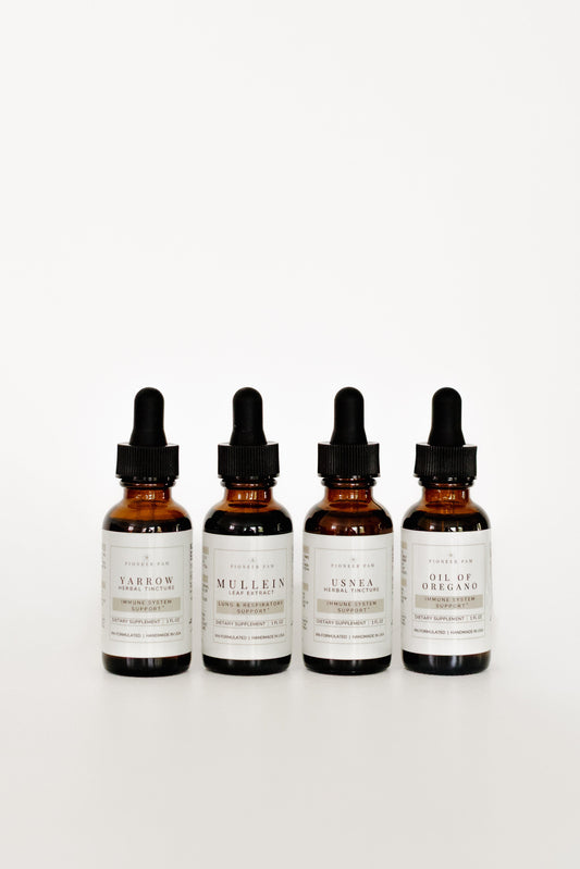 Four amber glass dropper bottles with black caps and white labels, arranged in a row on a clean white background. The labels show different scent names including Saffron, Mullein, Lunna, and Oil of Oregano.